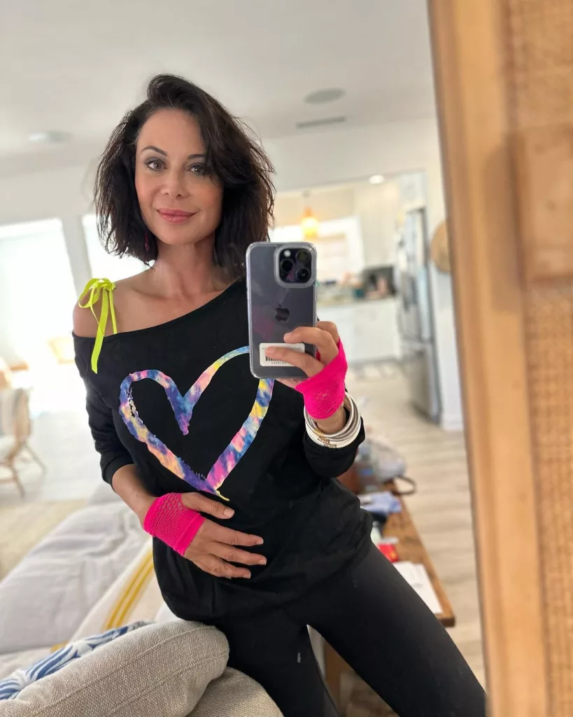 Catherine Bell taking a selfie wearing black off shoulder top.