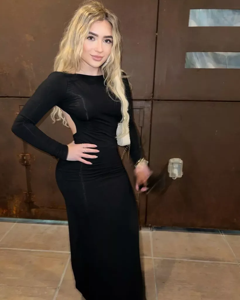 Faith wearing a black maxi dress and posing with her hand placing on her waist.