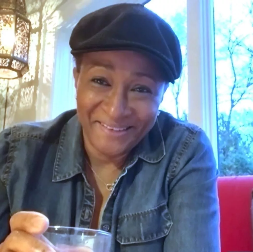 Wanda Sykes taking a drink wearing hat of black color