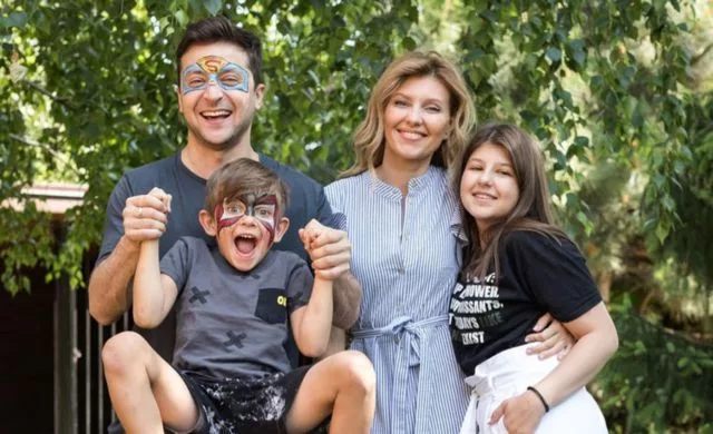 Kiril Zelenskiy with his family in the picture. He is wearing grey colored clothes.