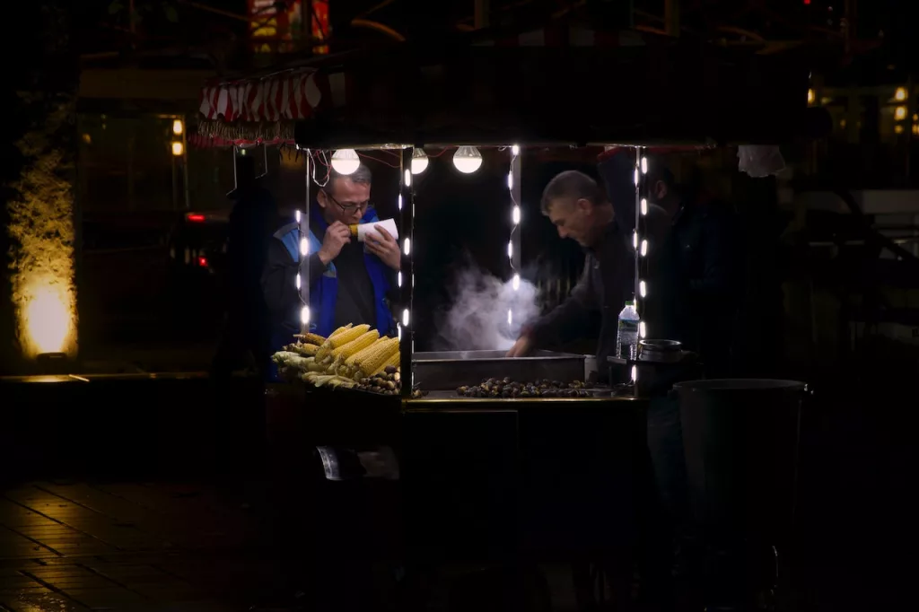 A Person at a Food Stand eating food at night.