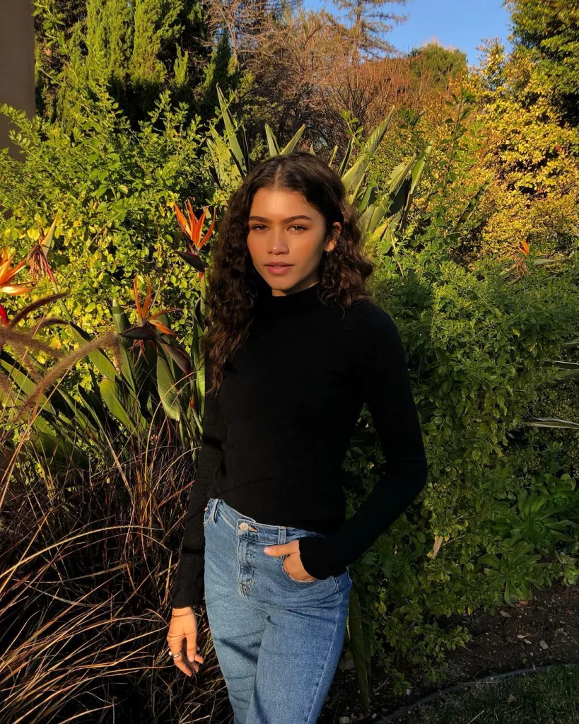 Zendaya wearing a black top and blue jeans.