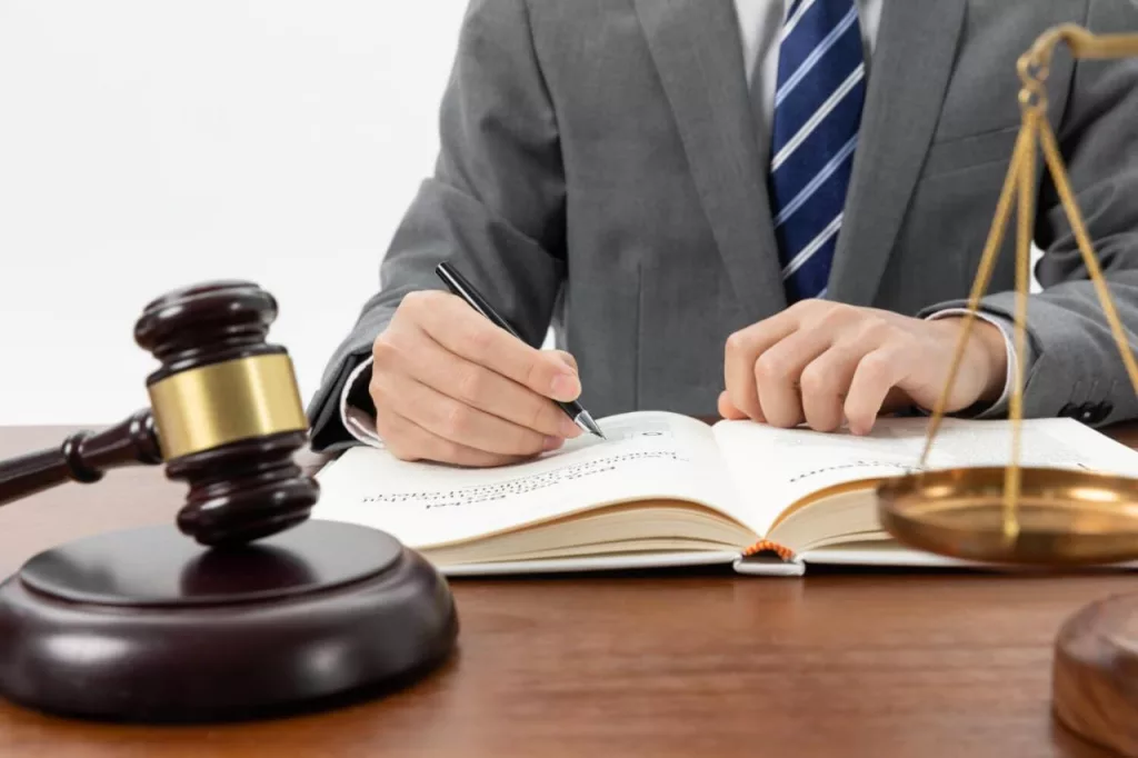 A man wearing grey suit and blue tie and writing in his book. 