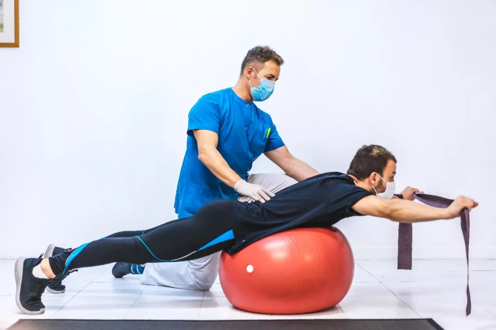A physiotherapist treating his patient using a red colored exercise ball
