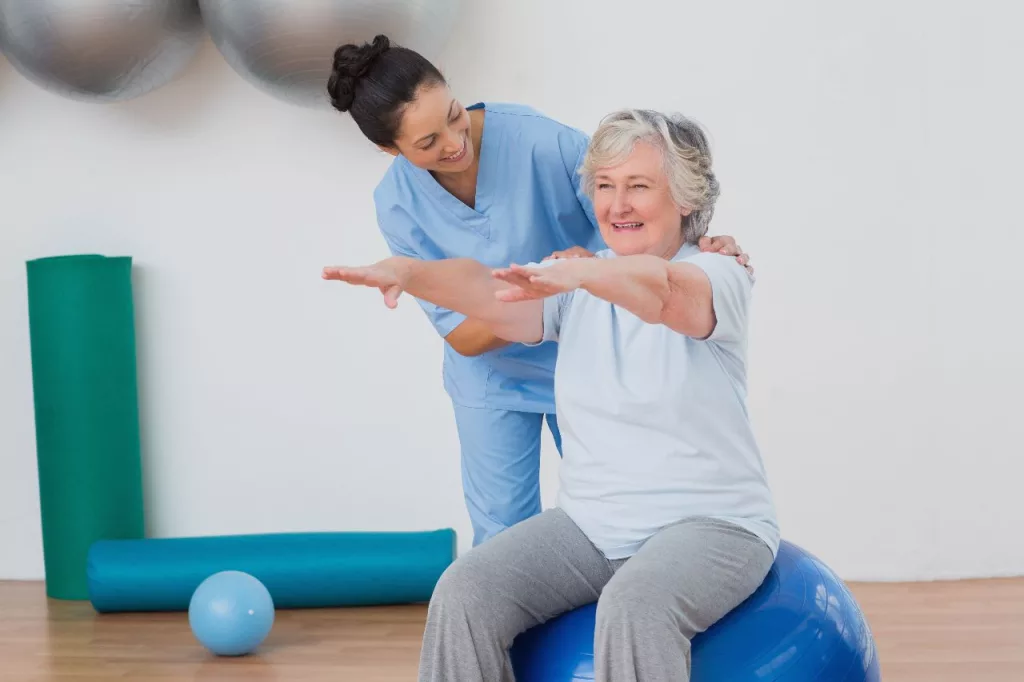 A female physiotherpaist treating an old woman using exercise ball.