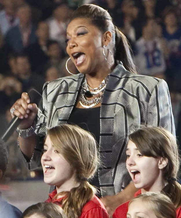 Queen Latifah singing on a stage with children.