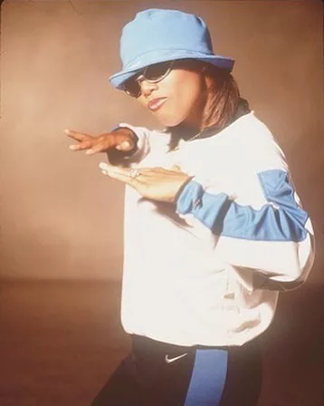 Queen Latifah posing in a blue cap and white sweatshirt. She is wearing a black lower.