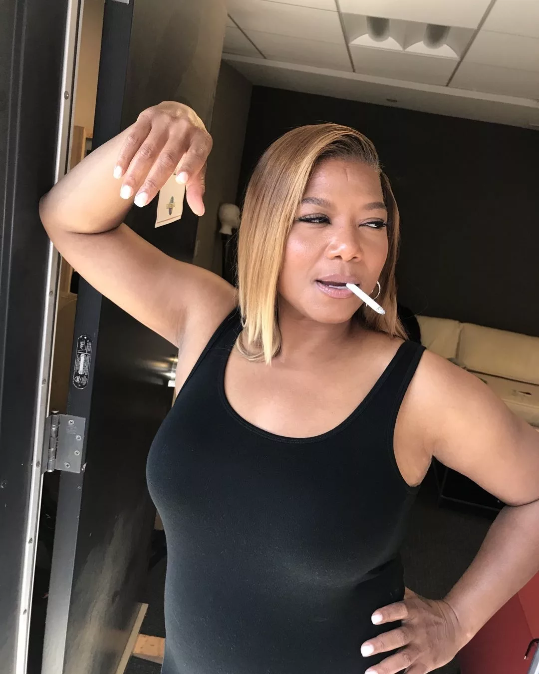 Queen Latifah wearing black sando and holding a cigarette and lighter.