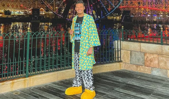 Ryan Seacrest wearing green colorful robe with black t-shirt and black printed lower. He is also wearing yellow colored shoes.