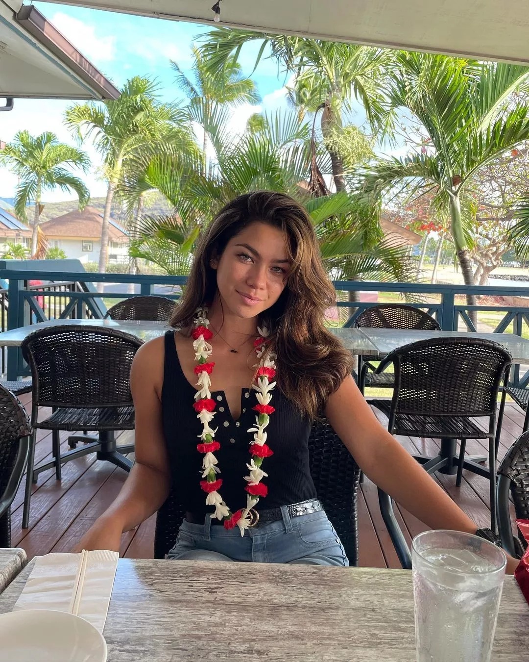 Kamalani posing in a restaurant and wearing black top blue jeans. She is also wearing a flower garland.
