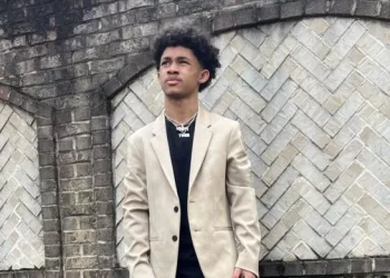 Dwayne wearing black shirt and jeans with light colored coat and sports shoes.