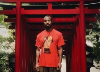 Michael B Jordan wearing a red colored t shirt and brown pants.